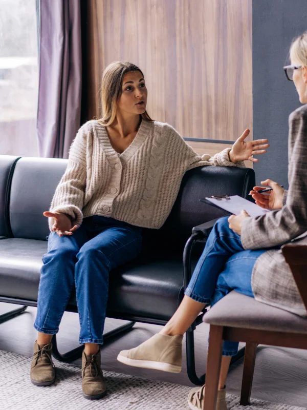 A young woman and her therapist talk while sitting on a couch.