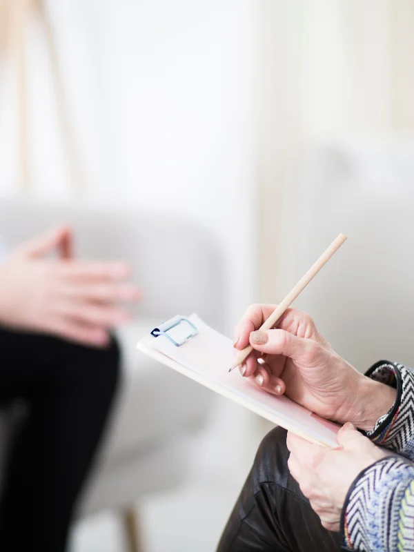 A therapist takes notes while listening to their client.